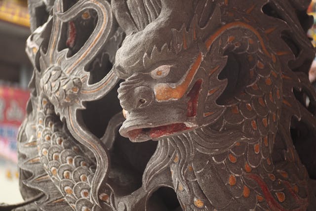 Artisan hand carving dragon tail details on wooden sculpture with traditional tools